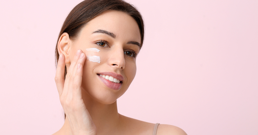 Beautiful,Young,Woman,Applying,Face,Cream,On,Pink,Background