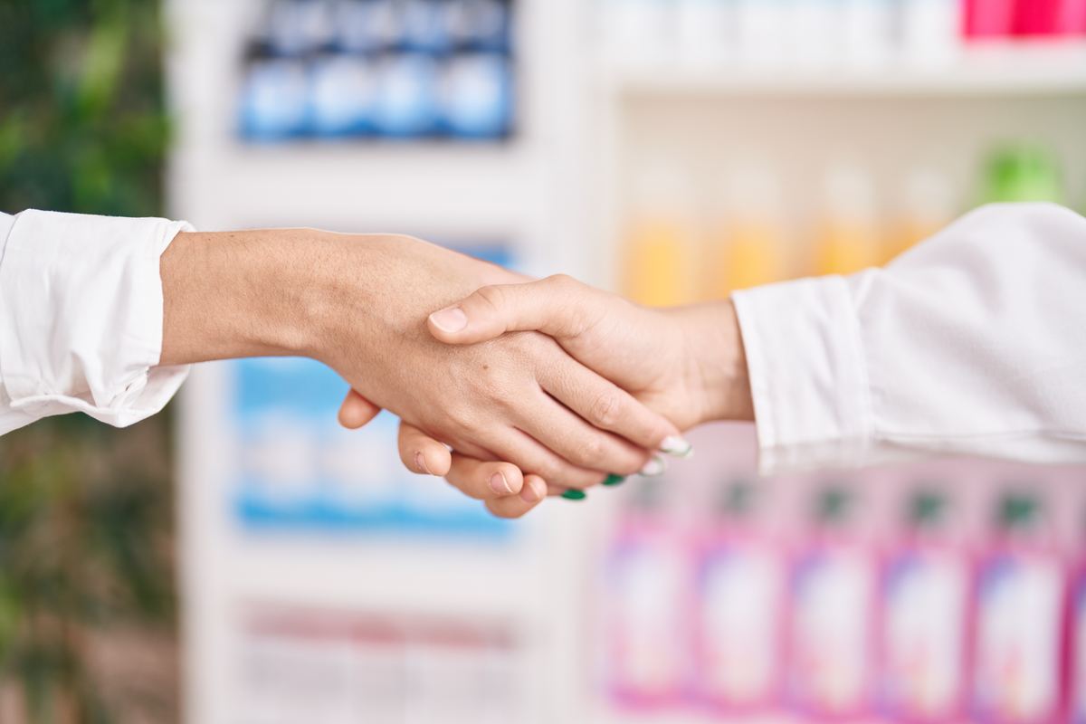 Pharmacist and franchise partner shaking hands in front of a pharmacy shelf